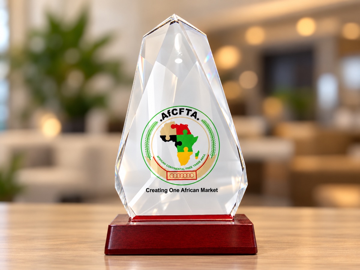 A faceted clear crystal award printed with a circular emblem and a map of Africa, on a polished red base, standing on a wooden table