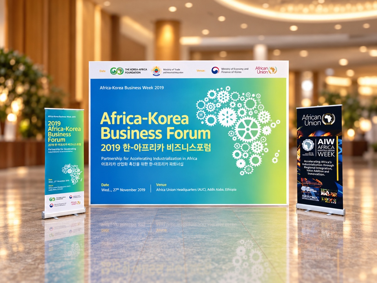 A large printed backdrop for a business forum with a gear and map graphic, flanked by two matching roll-up banners, on a polished floor in a hotel lobby