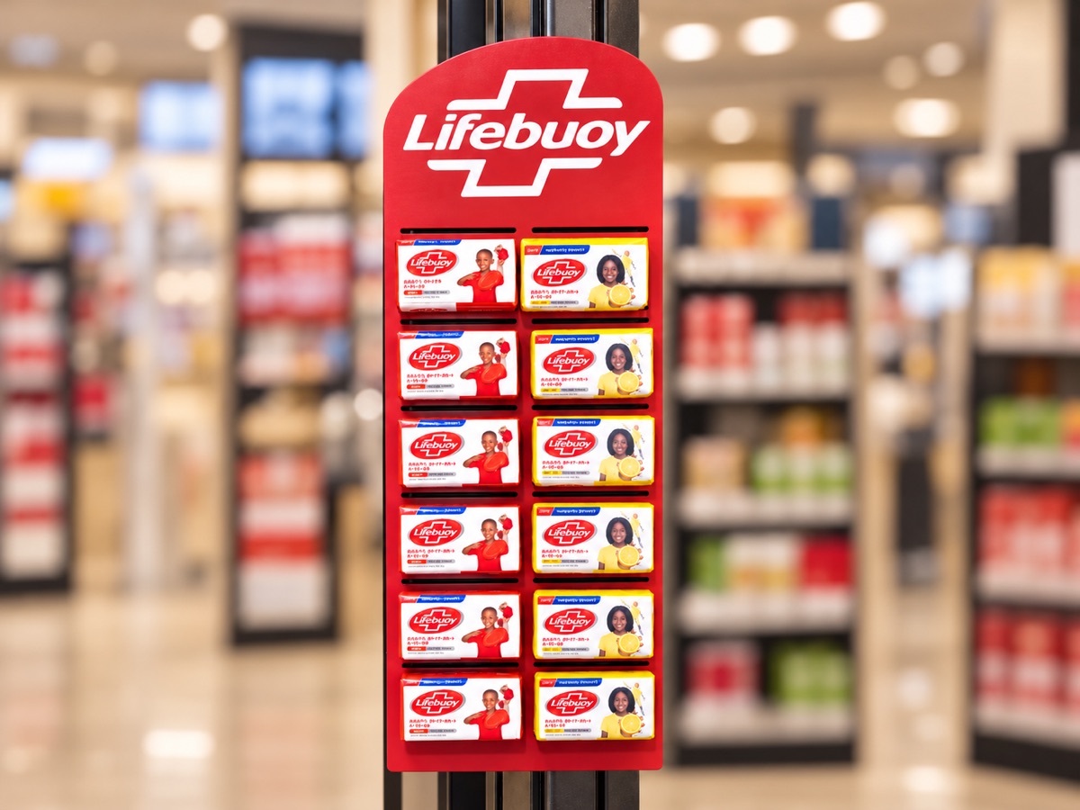 A tall red wall-mounted display strip with a shaped header, holding two columns of boxed soap, in a supermarket aisle