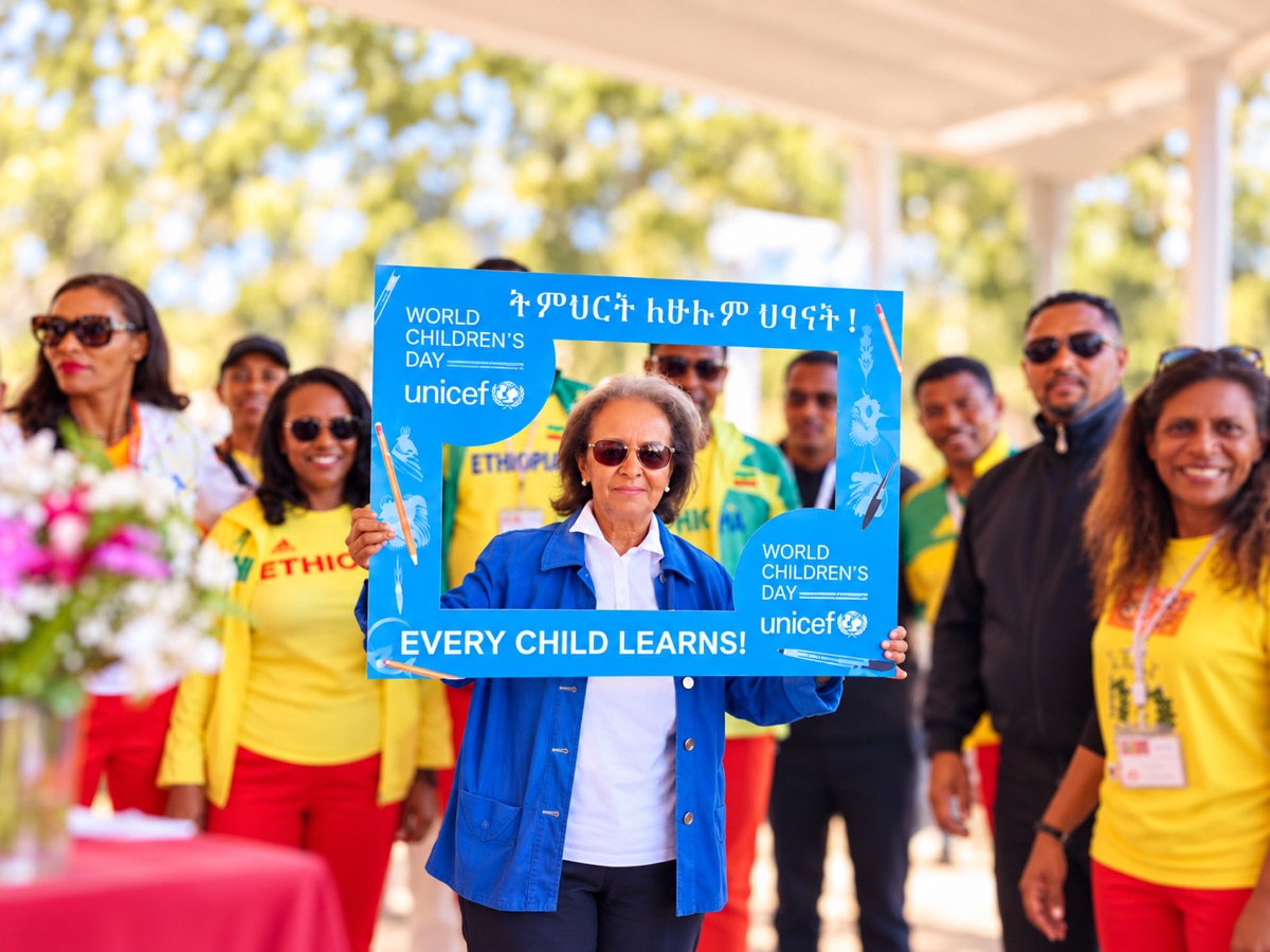 A group of guests at an outdoor event, one holding up a large blue branded photo-frame prop, smiling under a white canopy