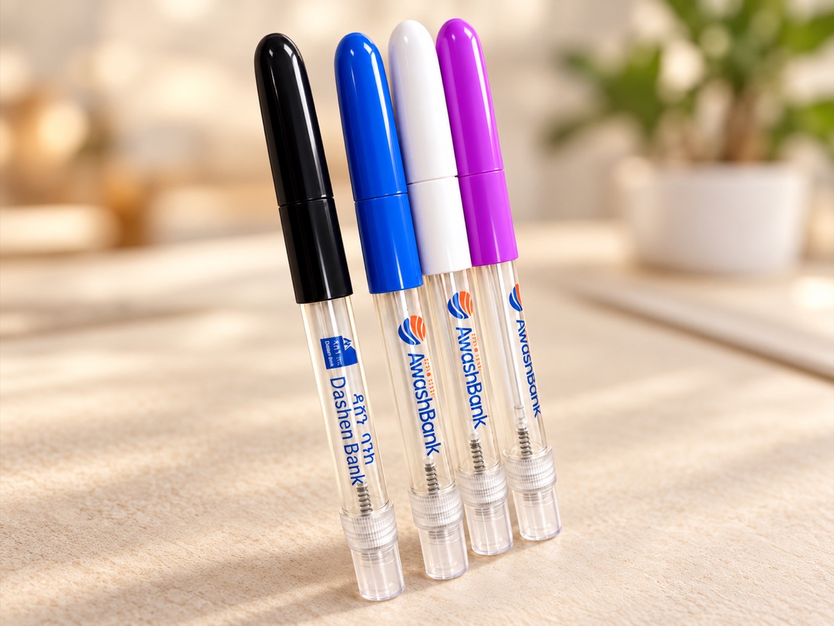 Four printed pocket spray pens with black, blue, white and purple caps, lying side by side on a light table